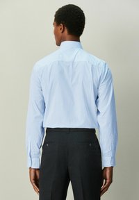 Camisa de vestir a rayas azul claro con cuello semiclasico, mangas largas y puños con botones, combinada con pantalones oscuros a medida.