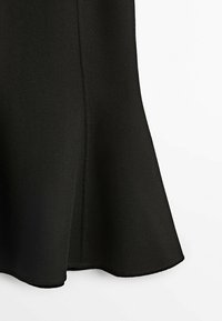 Ourlet de jupe évasée noire avec couture verticale visible et texture de tissu lisse sur fond blanc.