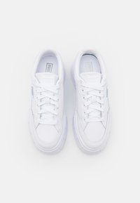 White sneakers with a smooth leather upper, flat laces, padded collar, and chunky rubber soles. Silver branding on the side.