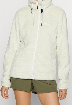 Biała, miękka bluza zapinana na zamek z kapturem i troczkami, noszona z oliwkowozielonymi szortami na osobie stojącej na jednolitym tle.