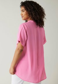 Camicetta rosa a maniche corte con pattern testurizzato, orlo arrotondato e vestibilità ampia. Progettata con scollatura a girocollo e tessuto morbido.