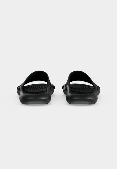Paire de sandales noires à enfiler avec semelles texturées et brides arrière réglables, vues de dos sur un fond uni.