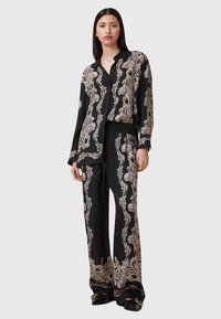 Conjunto de pijama em cetim preto com padrão de padrão cachemira em creme. Apresenta uma camisa com botões e calças com cintura elástica e pernas largas.