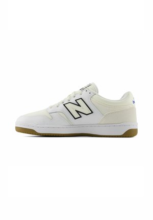 Weißer Sneaker mit niedrigem Schaft, schwarzem "N"-Logo, Kautschuksohle und Schnürung, seitlich auf weißem Hintergrund gezeigt.
