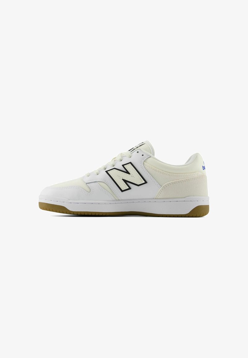 Witte lage sneaker met zwart "N"-logo, gumzool en veters aan de voorkant, zijaanzicht op een witte achtergrond.