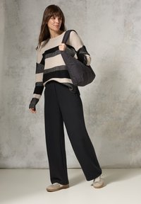 Maglione lavorato a maglia a righe beige e nere, pantaloni neri larghi, sneakers grigie e bianche, con una borsa a spalla imbottita nera.