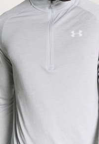 Hellegrau farbener langärmeliger Pullover mit Viertelreißverschluss, hergestellt aus einem glatten, leichten Stoff. Verfügt über ein weißes Logo auf der Brust und hat eine weiche Textur.