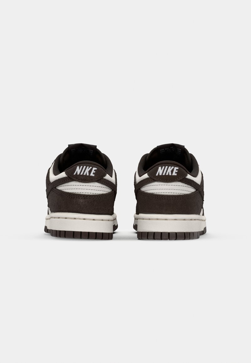 Sneaker in suede marrone con accenti bianchi, dotate di un tallone in pelle, una suola intermedia testurizzata e un marchio prominente sul retro del tallone.