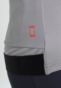 Camiseta atlética gris con una tela texturizada, que presenta un diseño de contorno de smartphone rojo en el costado y un dobladillo negro en la parte inferior.