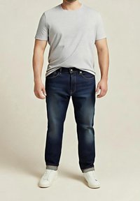 T-shirt gris à manches courtes, jean en denim bleu foncé avec décoloration légère, et baskets blanches. Coupe standard et design classique avec détails de coutures.