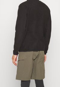 Maglia a maniche lunghe in pile nero con una texture liscia, abbinata a pantaloni cargo verdi oliva con tasche laterali e una vestibilità comoda.
