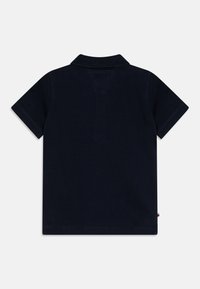 Tumši zila īsām piedurknēm polo krekls ar ribota apkakli, redzamām šuvju detaļām zem apkakles un mazu sānu birku uz vienkrāsaina fona.