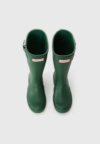 Grønne gummistøvler med høyglanset overflate, rund tå og justerbar stropp bak. Har en rød og hvit Hunter-logo.