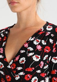 Černé květinové šaty s bílými, růžovými a červenými květy, hlubokým výstřihem do V a zdobením na ramenou. Měkká textura látky.