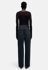 Zwart top met lange mouwen gecombineerd met hoge taille, wijd uitlopende donkere spijkerbroek met twee achterzakken en een rafelige zoom.