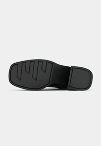 Semelle noire d'une chaussure formelle avec un motif de bande de roulement texturé et un petit talon rectangulaire, vue du dessous.