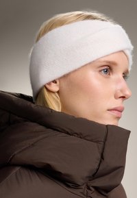 Bandeau en tricot blanc avec un design torsadé et une texture lisse, assorti à une veste matelassée marron avec un col haut et une surface matelassée.
