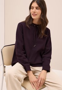 Donkerpaarse sweatshirt met een hoge hals, trekkoorddetails, lange mouwen, ribgebreide manchetten, gecombineerd met lichtbeige broek.