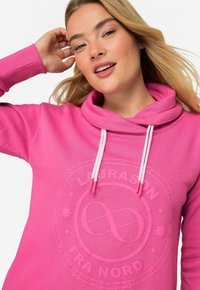 Felpa hot pink con un grande logo in rilievo al centro. Presenta un cappuccio con lacci bianchi e polsini a coste. Tessuto morbido.