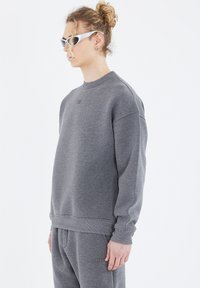 Grauer Sweatshirt mit rundem Ausschnitt und überschnittenen Schultern, gefertigt aus weichem Material. Verfügt über ein minimalistisches Branding auf der Brust und gerippte Ärmelbündchen.