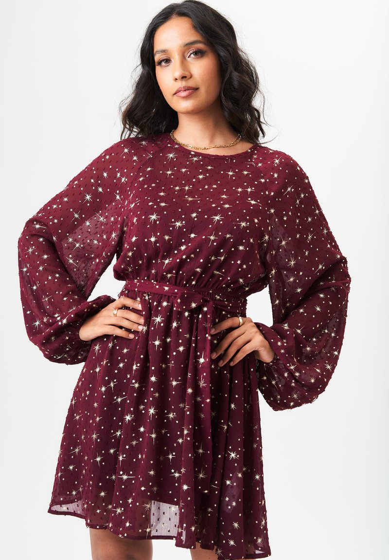 Burgundy dress with long puff sleeves, belted waist, and star-like metallic patterns. Sheer fabric adds texture and lightness.