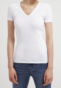 Vit kortärmad V-ringad t-shirt i blandad bomull med en figursydd design, kombinerad med blå denimjeans. Slät textur.