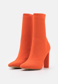 Bottes de cheville orange en tissu texturé avec un bout pointu et un talon haut de couleur unie. Design sans couture sans fermetures visibles.