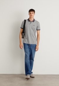 Γκρι ριγέ πόλο μπλούζα με αντίθετο γιακά, συνδυασμένη με μπλε τζιν και γκρι παπούτσια. Το μοντέλο κρατάει μια μαύρη τσάντα κράνους.