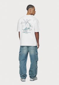 Biela tričko s grafiku citróna a textom "Superior Quality Pegador" na chrbte, doplnené svetlo modrými voľnými cargo nohavicami.