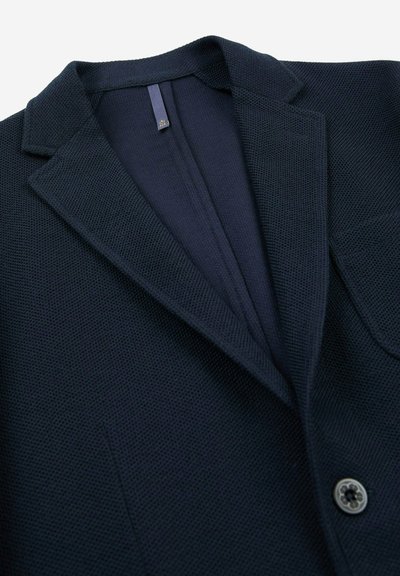 Blazer navy in tessuto testurizzato, con rever a punta, chiusura a singolo bottone e taschino sul petto. Dettagli di cucitura distintivi sul colletto.