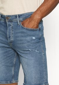 Pantalones cortos de mezclilla en azul claro con una textura ligeramente desgastada. Presentan un diseño clásico de cinco bolsillos y un dobladillo vuelto.