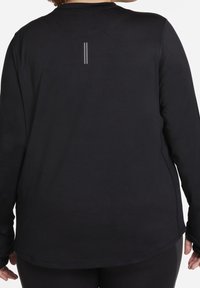 Czarna sportowa koszulka z długim rękawem, z zaokrąglonym dołem, miękką fakturą i odblaskowymi paskami z tyłu. Dopasowany krój z elastycznego materiału zapewniający swobodę ruchów.