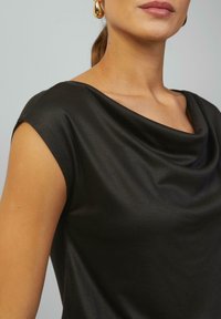 Černý top s kapucí a krátkými rukávy; hladká textura a splývavý design. Minimalistický styl, vhodný pro různé příležitosti.