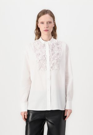 Hvit langermet skjorte med et strukturert, lys rosa brodert panel foran, med mandarin krage og knappelukking.