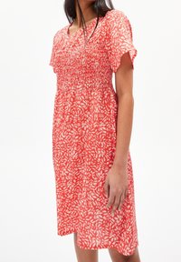 Šaty s červeným vzorem, s nařaseným živůtkem, krátkými rukávy a uvolněným střihem. Jsou vyrobené z lehké texturované látky s motivy listů.