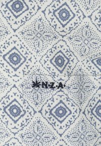 Blauw en wit gestreepte stof met diamanten en bloemmotieven, met een geborduurd etiket onderaan met de tekst "N.Z.A." in zwart.