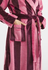 Fleece badrock med vertikala ränder i rosa och mörklila. Har ett knytbälte, framfickor och en mjuk textur.