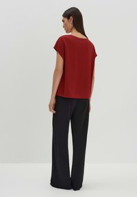 Rotes kurzärmliges Oberteil mit lockerer Passform, kombiniert mit schwarzen weiten Hosen, beide mit glatter Textur und schlichten Designs.
