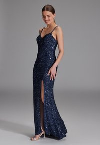Robe en sequins bleu marine scintillante au design ajusté, avec une fente haute sur la cuisse et des fines bretelles, offrant une texture lisse et une forme élégante.