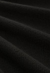 Gros plan sur un tissu côtelé noir doux avec des plis délicats et une texture légèrement duveteuse.