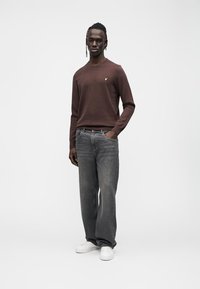 Brown knit sweater with a round neckline, paired with loose-fitting grey denim jeans and white sneakers. Features a small logo on the sweater.