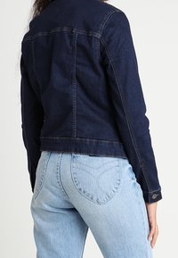 Tmavě modrá džínová bunda s přiléhavým střihem, s prošitými švy, zapínáním na knoflíky a zkrácenou délkou, doplněná světle modrými džínami.