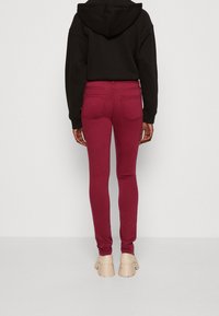 Bordeaux skinny jeans met een hoge taille, gemaakt van een zacht denim materiaal, voorzien van achterzakken en een naadloos ontwerp. Gecombineerd met tan kleurige schoenen.
