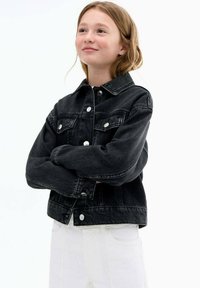 Črna denimska jakna s ovratnikom, sprednjimi žepi in srebrnimi gumbi. Ima sproščen kroj in dolge rokave. V kombinaciji z belimi kavbojkami.