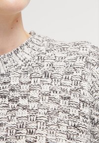 Stickad tröja i svart och vitt med en texturerad, vävd mönstring. Har en rundad halsringning och mjukt, tjockt garnmaterial.