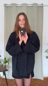 Zwarte textuur portemonnee met een gouden sluiting, vastgehouden door een persoon in een loszittend zwart shirt, voor een neutrale achtergrond met groen. 