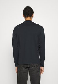 Czarny t-shirt z długim rękawem wykonany z bawełny, z prostym okrągłym dekoltem i gładką powierzchnią. Noszony z ciemnymi dżinsami.