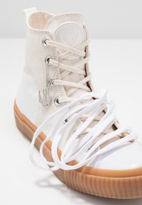 Höga sneakers med en beige tygovandel, vit gummitå och brun gummisula. Utrustad med metallöglor och vita snören.