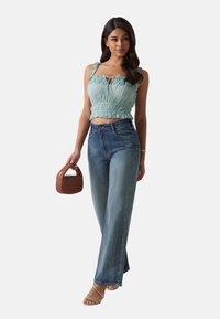 Light blue cropped top with lace detail, high-waisted faded blue jeans, and a brown woven handbag. Model wears transparent heeled sandals.