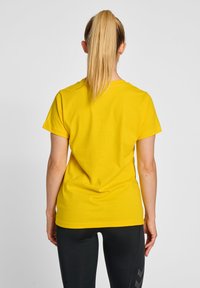 Geel katoenen t-shirt met korte mouwen, ronde halslijn en een gladde textuur, gedragen met zwarte sportbroeken met een diagonaal patroon.